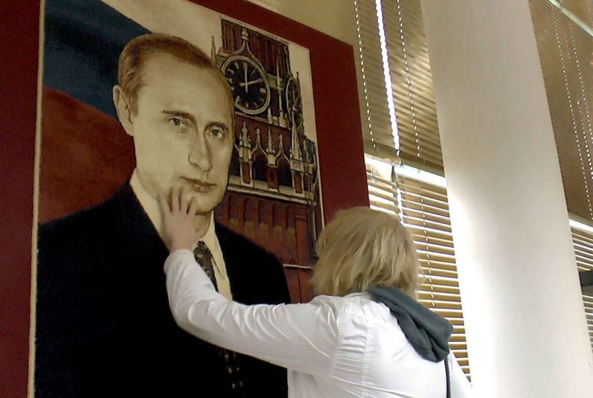 žena se rukou dotýká obrazu Vladimíra Putina na zdi